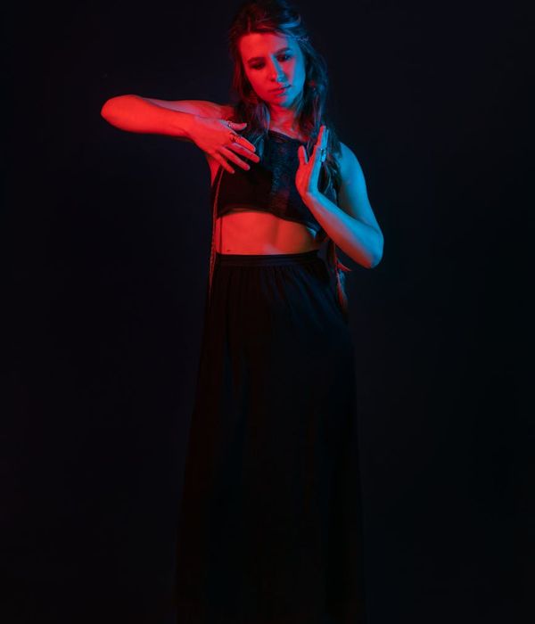 Woman performing a fluid yoga pose in a dark studio with pink light.
